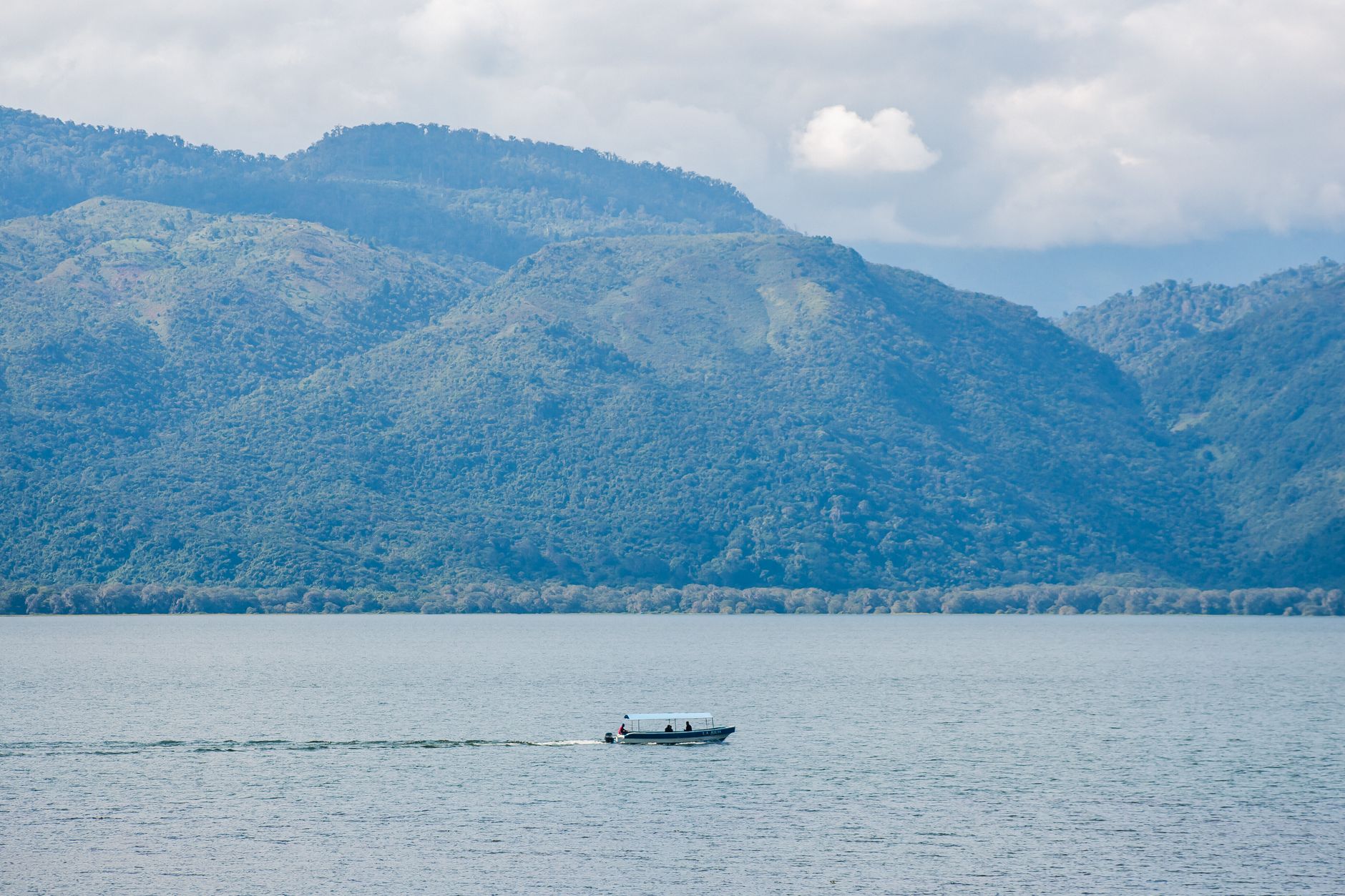 A tranquil view of a boat on a lake surrounded by lush mountains in Honduras.