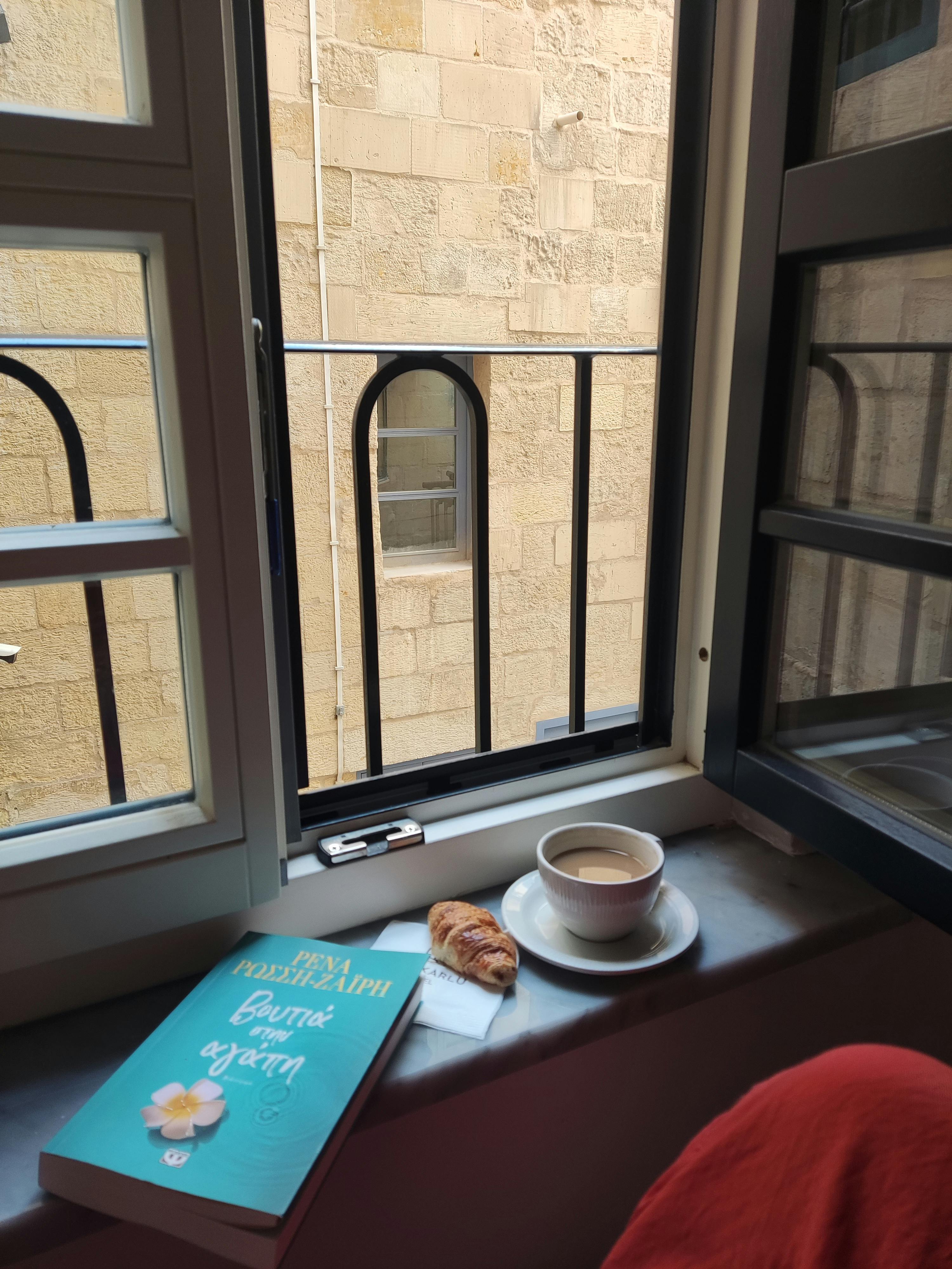 Serene morning scene with coffee, book, and croissant by an open window.