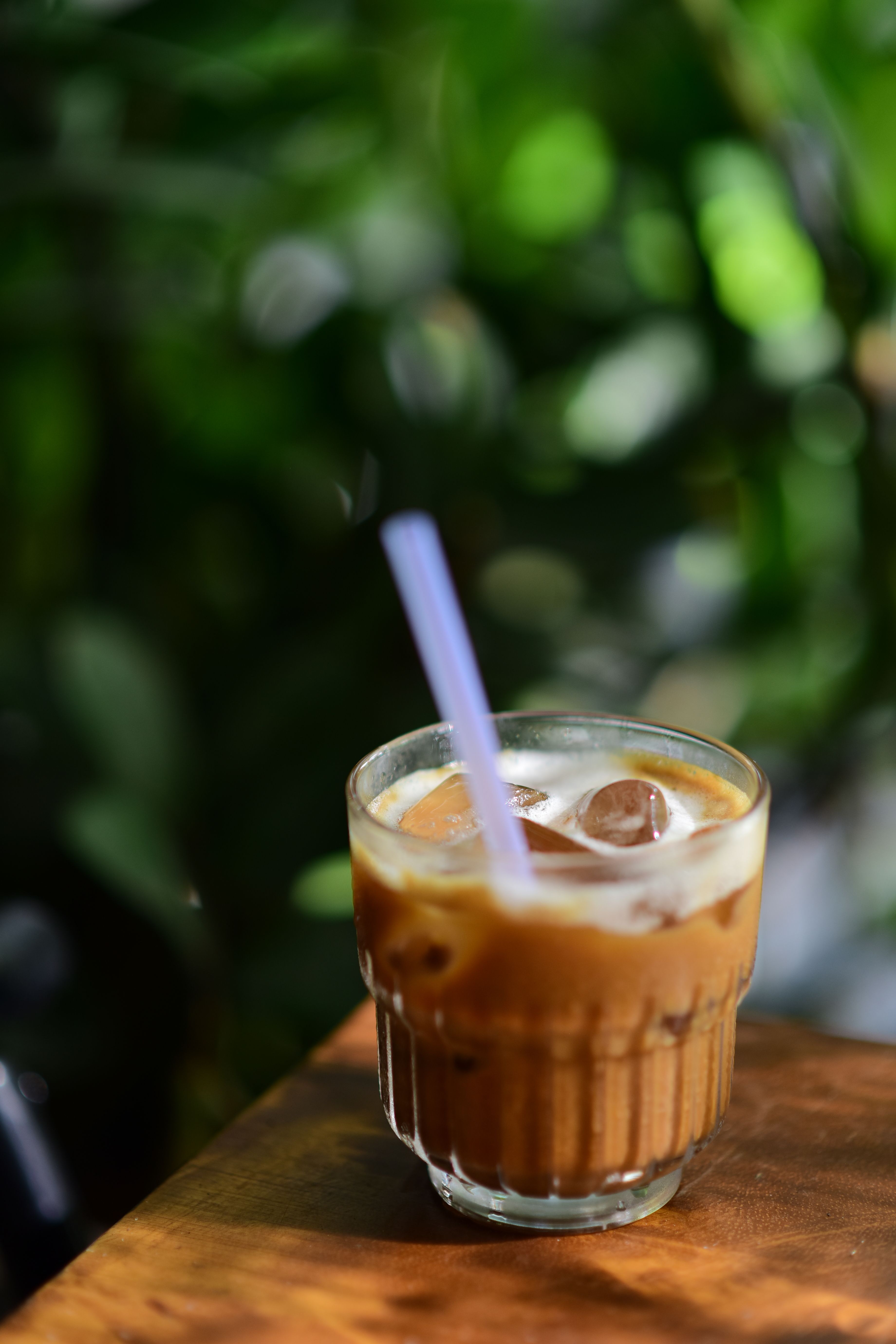 Chilled iced coffee on a wooden table against a lush green background, perfect for refreshing moments.