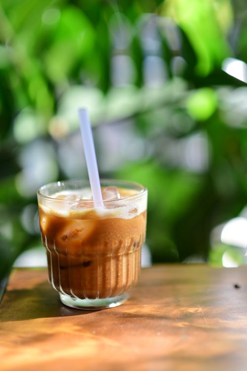 Free A glass of iced coffee with straw, set against blurred greenery, exuding a refreshing vibe. Stock Photo