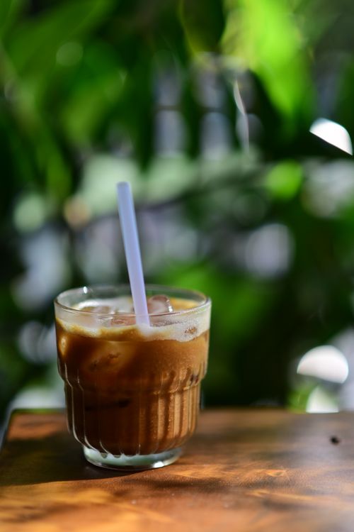 Free Close-up of a refreshing iced coffee in sunlight with blurred green leaves. Stock Photo