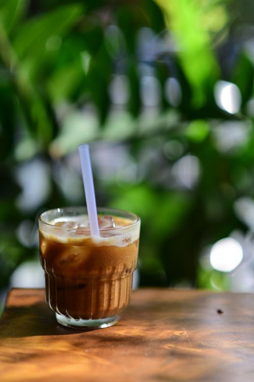Free Iced coffee in a glass with straw on a wooden table outside in a sunlit garden. Stock Photo