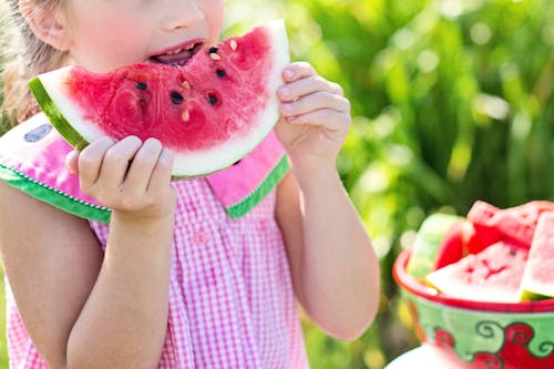 Free Girl Eating Sliced Watermelon Fruit Beside Table Stock Photo