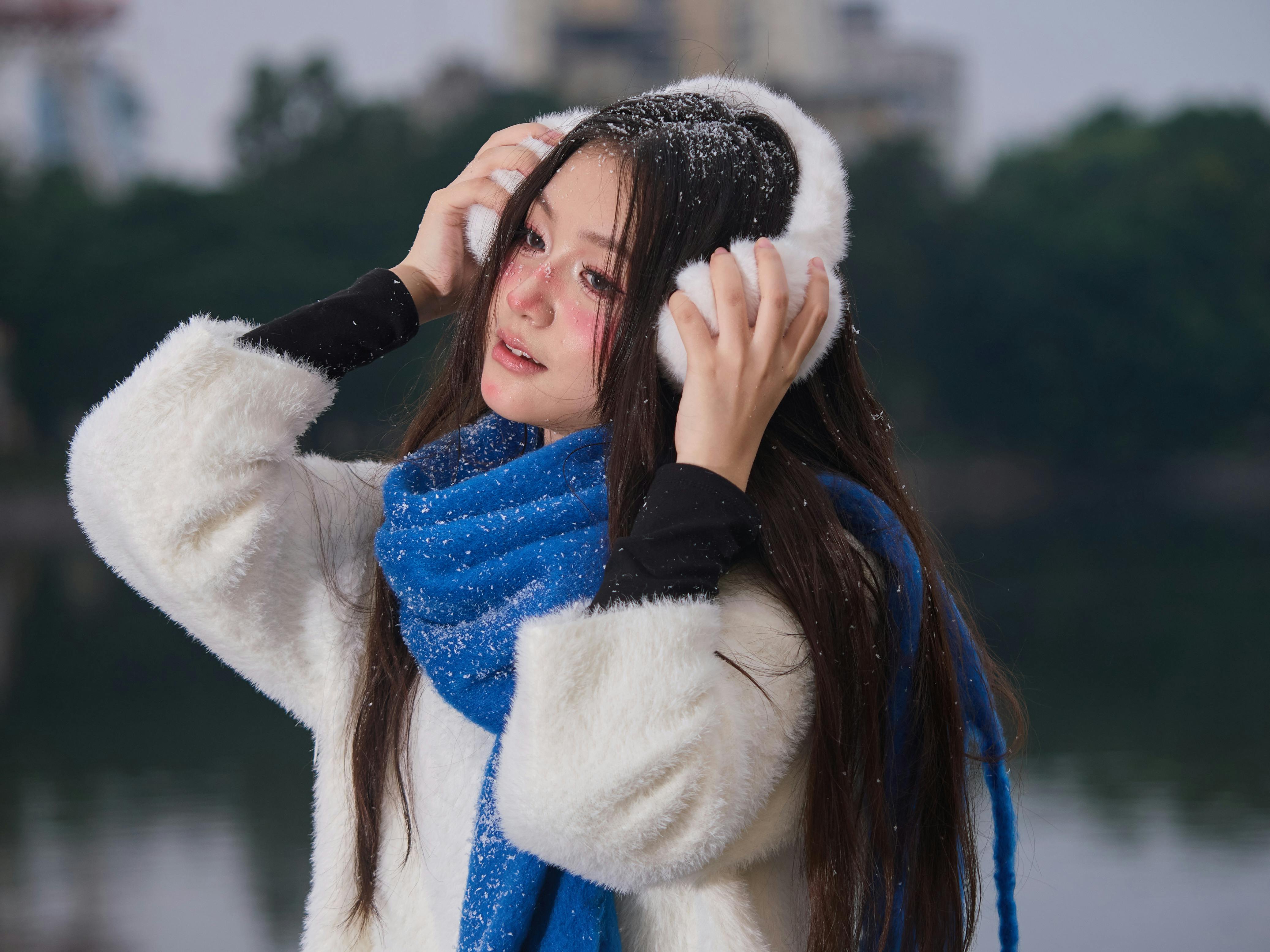 Ücretsiz Beyaz palto ve mavi atkı takmış genç bir kadın, Vietnam'ın Hanoi şehrinde yapay karın tadını çıkarıyor. Stok Fotoğraflar