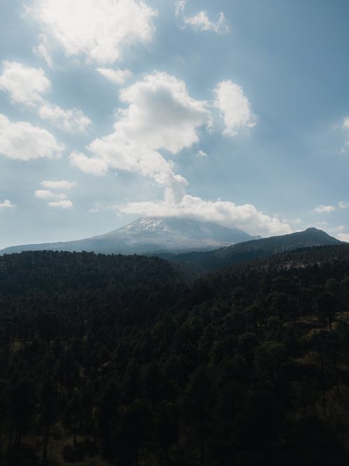Free A stunning aerial view of Popocatépetl Volcano surrounded by lush forests under a bright blue sky. Stock Photo