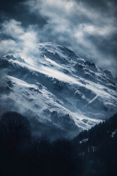 Moody winter scene of a snow-covered mountain peak with dramatic clouds.
