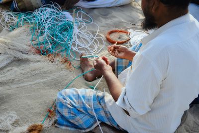A fisherman seated on the ground knitting a fishing net