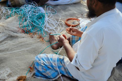 Free A fisherman meticulously knits a fishing net on the sandy beach of Cox's Bazar, Bangladesh. Stock Photo