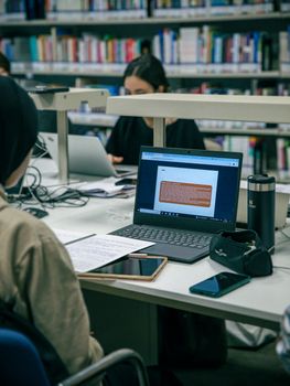 Students studying with laptops and books in a modern library environment, focused and engaged.