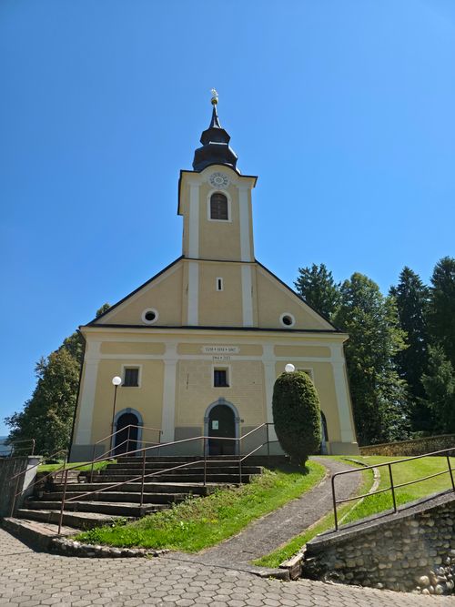 Free Picturesque Slovenian church surrounded by lush greenery under a clear blue sky. Stock Photo