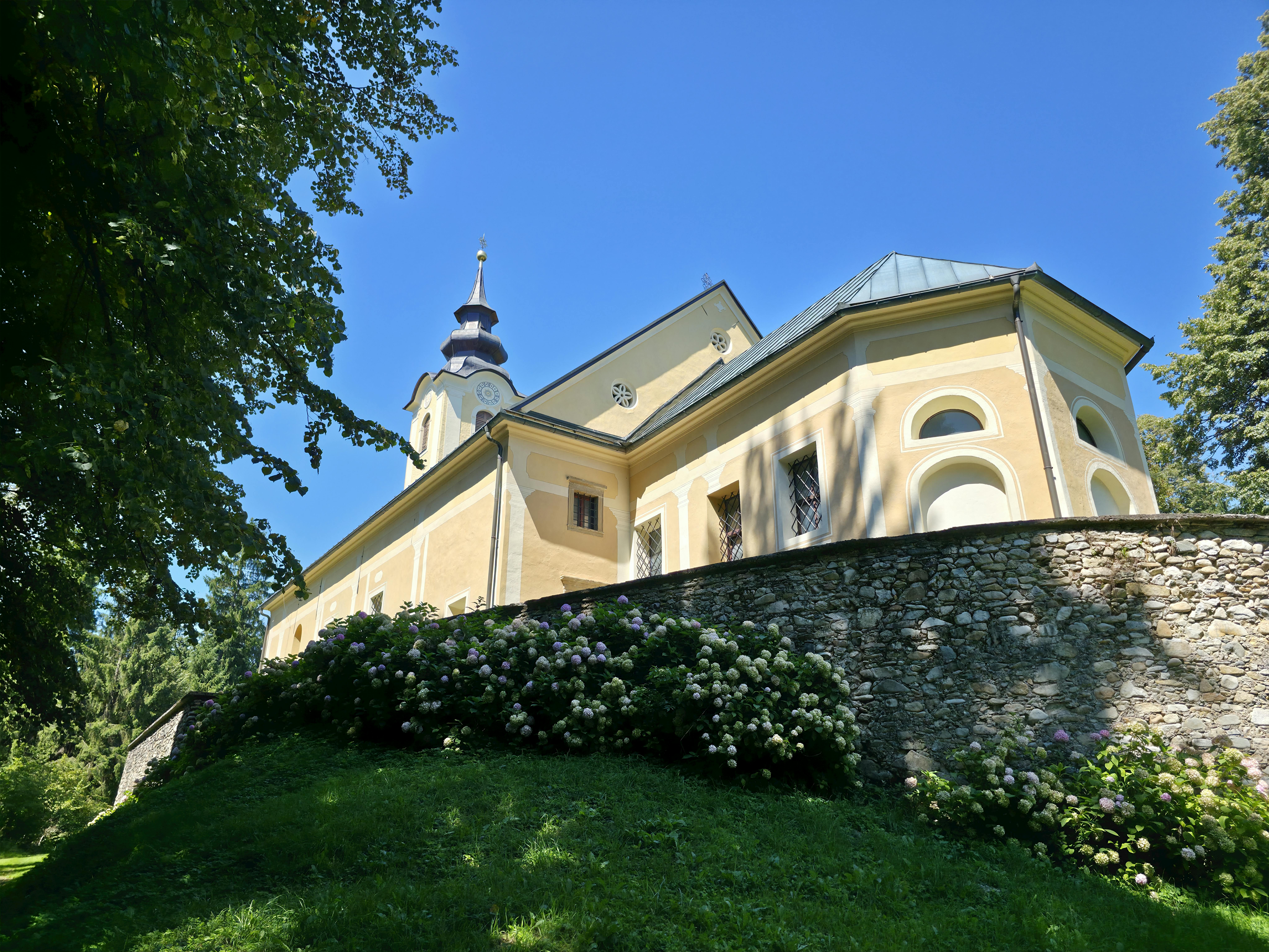A picturesque ancient church surrounded by lush greenery under a vibrant blue sky in summer