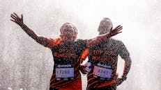 马拉松比赛中，两名跑步者伸出双臂，在冷却喷雾下庆祝