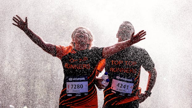 马拉松比赛中，两名跑步者伸出双臂，在冷却喷雾下庆祝