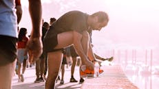 男子在户外跑步前系鞋带，旁边放着一瓶水