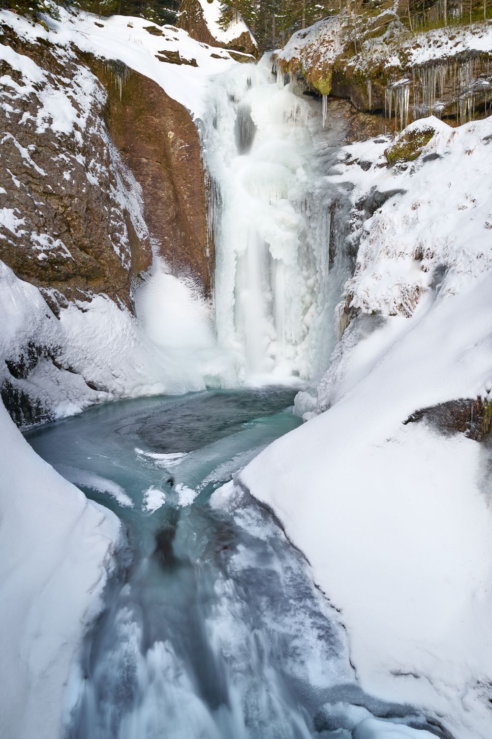 Snow-rimmed frozen waterfall in winter landscape