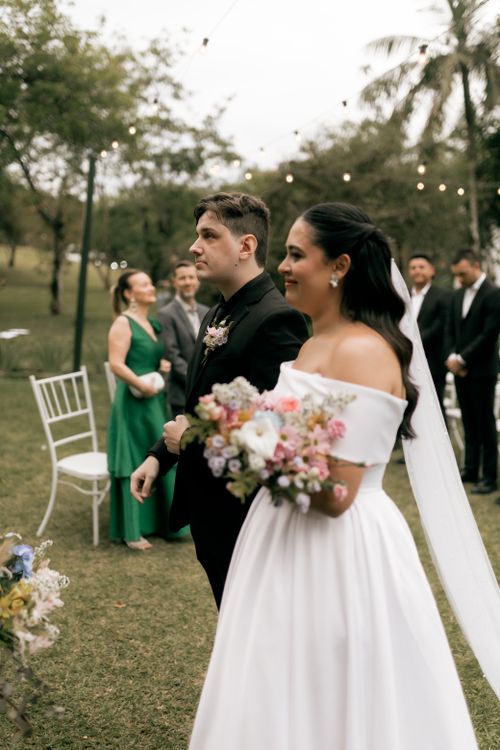 Free Bride and groom at an outdoor wedding ceremony, holding a vibrant floral bouquet. Stock Photo