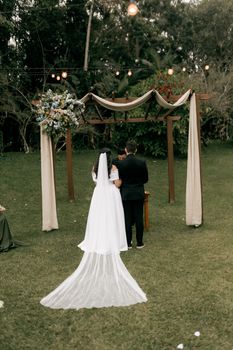 Bride and groom standing under a decorated arbor during an outdoor wedding ceremony.