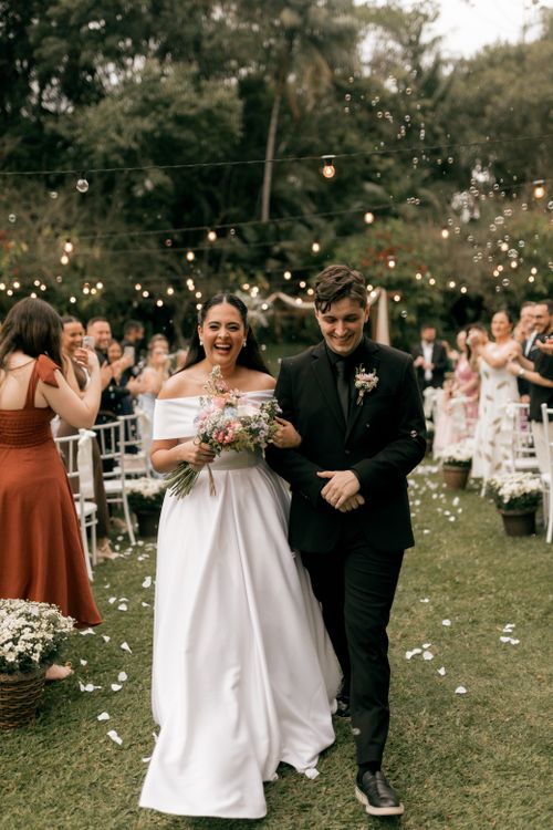 Free Bride and groom walking down the aisle, beaming with happiness at an outdoor wedding under string lights. Stock Photo