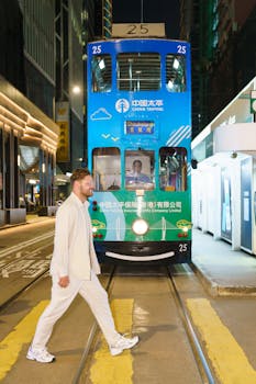 A man in white walks at night in front of a blue Hong Kong tram.