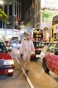 Man walking on lively nighttime street with bright city lights and traffic.