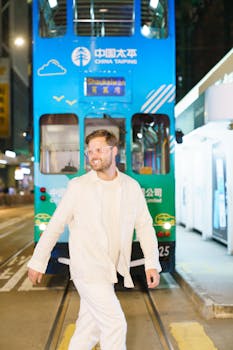 A man in white walks past a bright blue tram on a bustling street in Hong Kong at night.