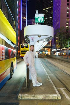 Man standing at bus stop on vibrant city street at night.
