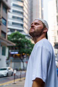 Casual man in white shirt and cap looking up in a vibrant city street.