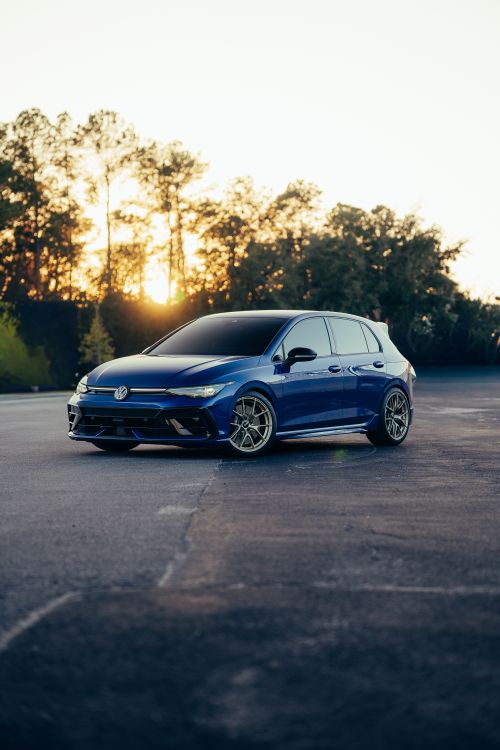 Free A sleek blue car parked in an empty lot at sunrise, surrounded by trees. Stock Photo
