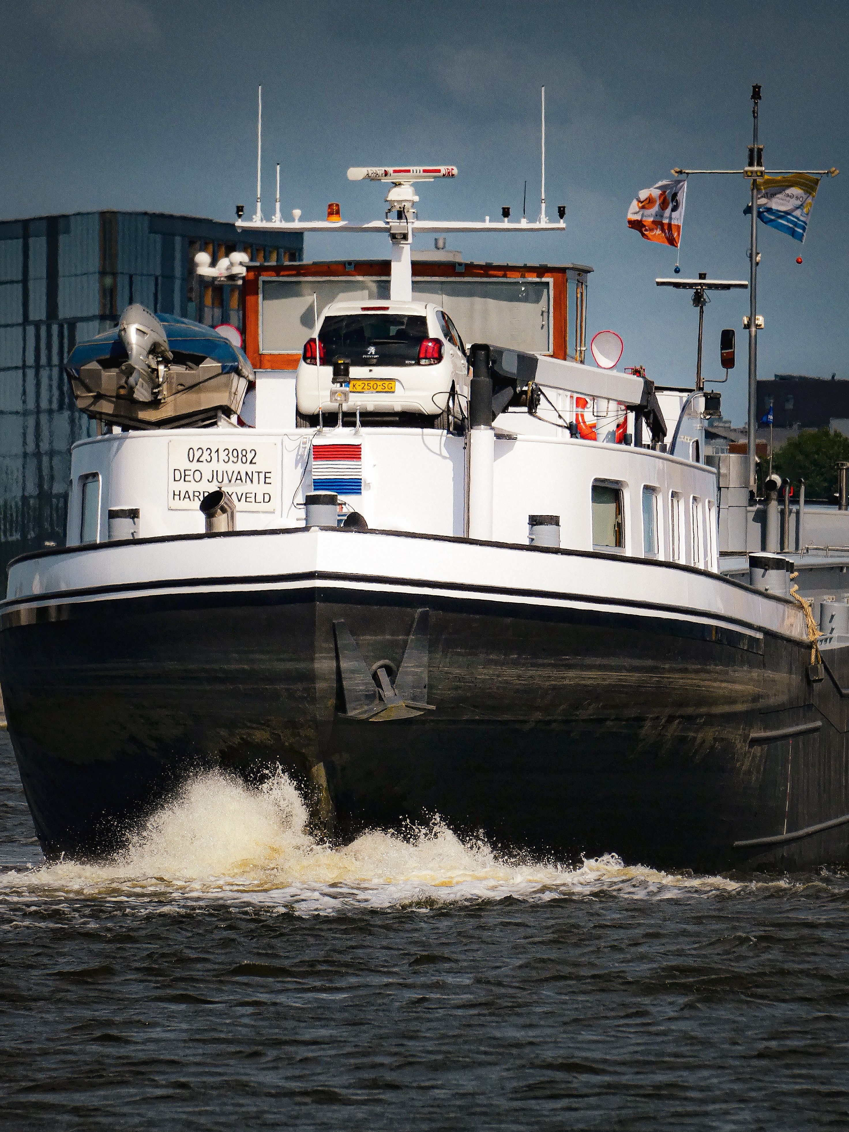 Front view of a cargo ship navigating through a city river under a cloudy sky.