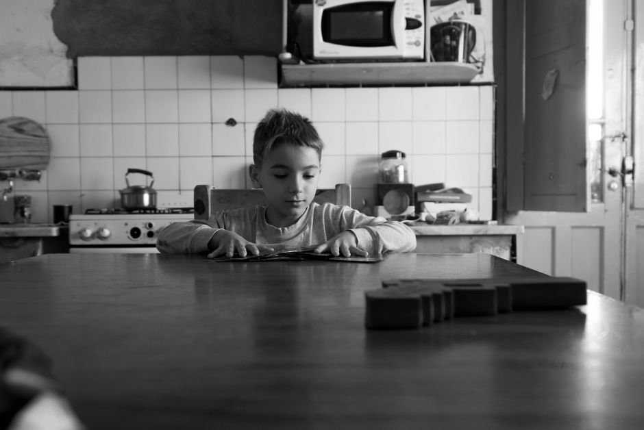 Young child reading at a table in a vintage kitchen setting.