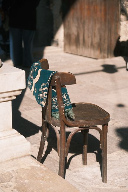 Sunlit vintage wooden chair draped with an artistic blue patterned blanket outdoors.