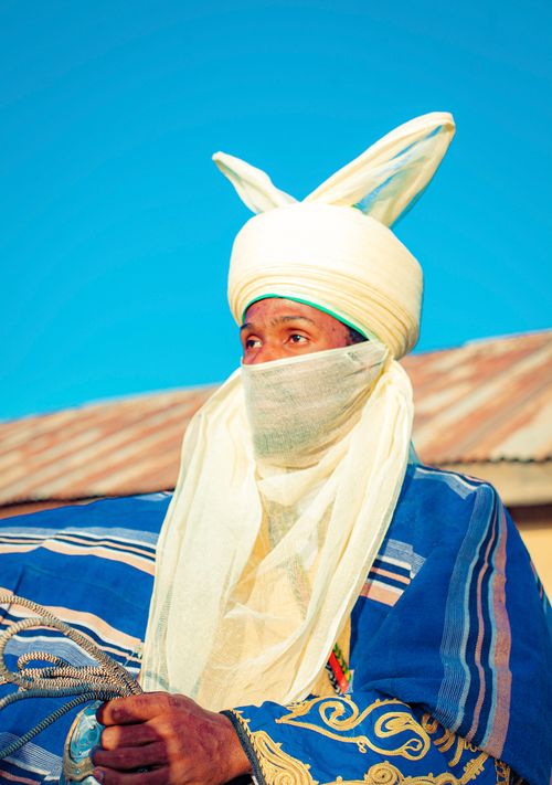 Free Man in traditional Hausa clothing with decorative turban in vibrant colors against a clear blue sky. Stock Photo