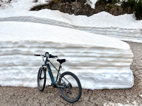 Bicycle stands against layered snow in Italian mountain terrain, showcasing winter's beauty.