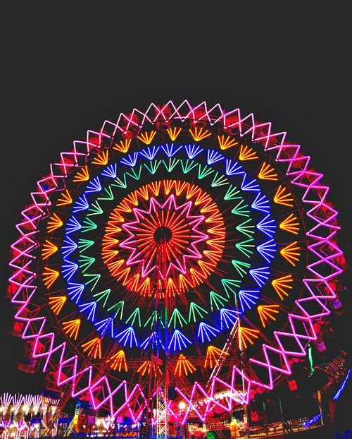 Free A mesmerizing Ferris wheel illuminated with vibrant neon lights against the night sky. Stock Photo