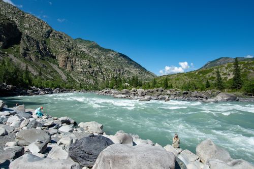 Free Pristine mountain river flowing through rugged terrain under a clear blue sky with a few people nearby. Stock Photo