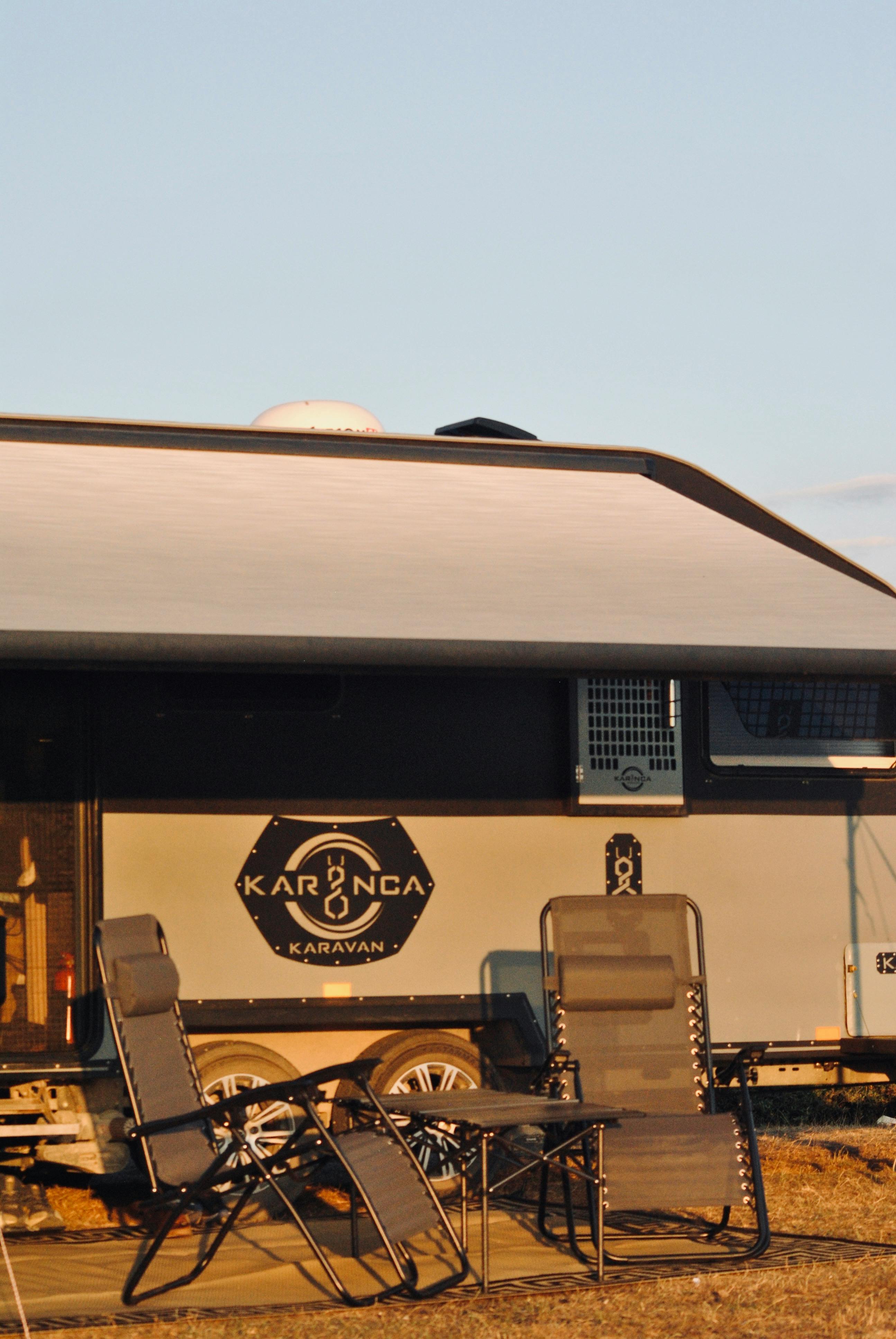 Cozy outdoor setup with chairs beside a caravan during sunset, perfect for camping vibes.
