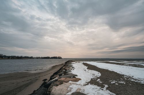 Free Peaceful winter beach scene with snowy shoreline and sunset sky. Stock Photo