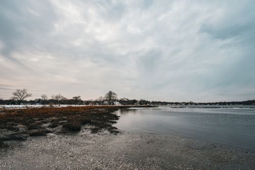 Free A calm coastal scene with a reflective shoreline under cloudy skies at daytime. Stock Photo