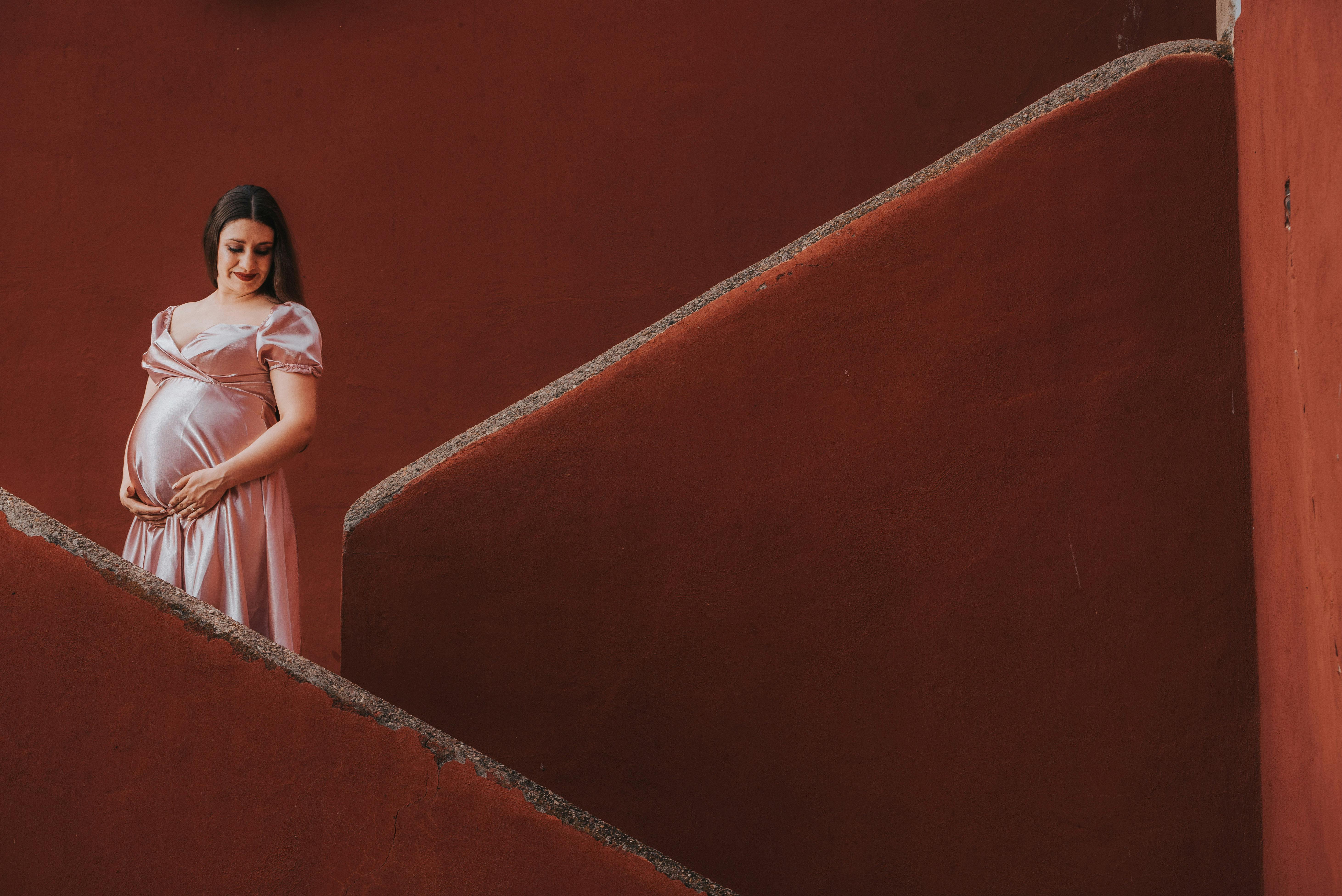 Gratuit Une femme enceinte, vêtue d'une robe rose, se tient gracieusement sur un escalier rouge. Photos
