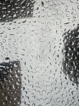 Close-up of raindrops on glass creating an abstract and moody view.