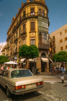 Elegant historic architecture in Seville, Spain, showcasing vibrant street life and classic cars.