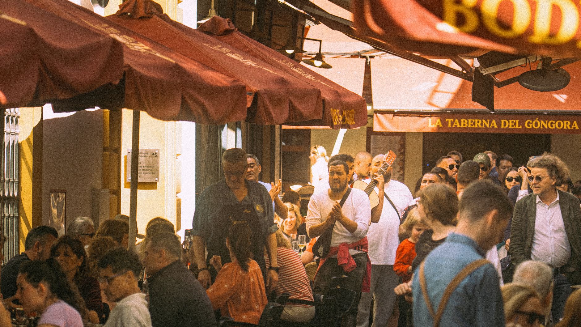 Druk terras in een Spaanse stad tijdens een voetbalavond met grote schermen.