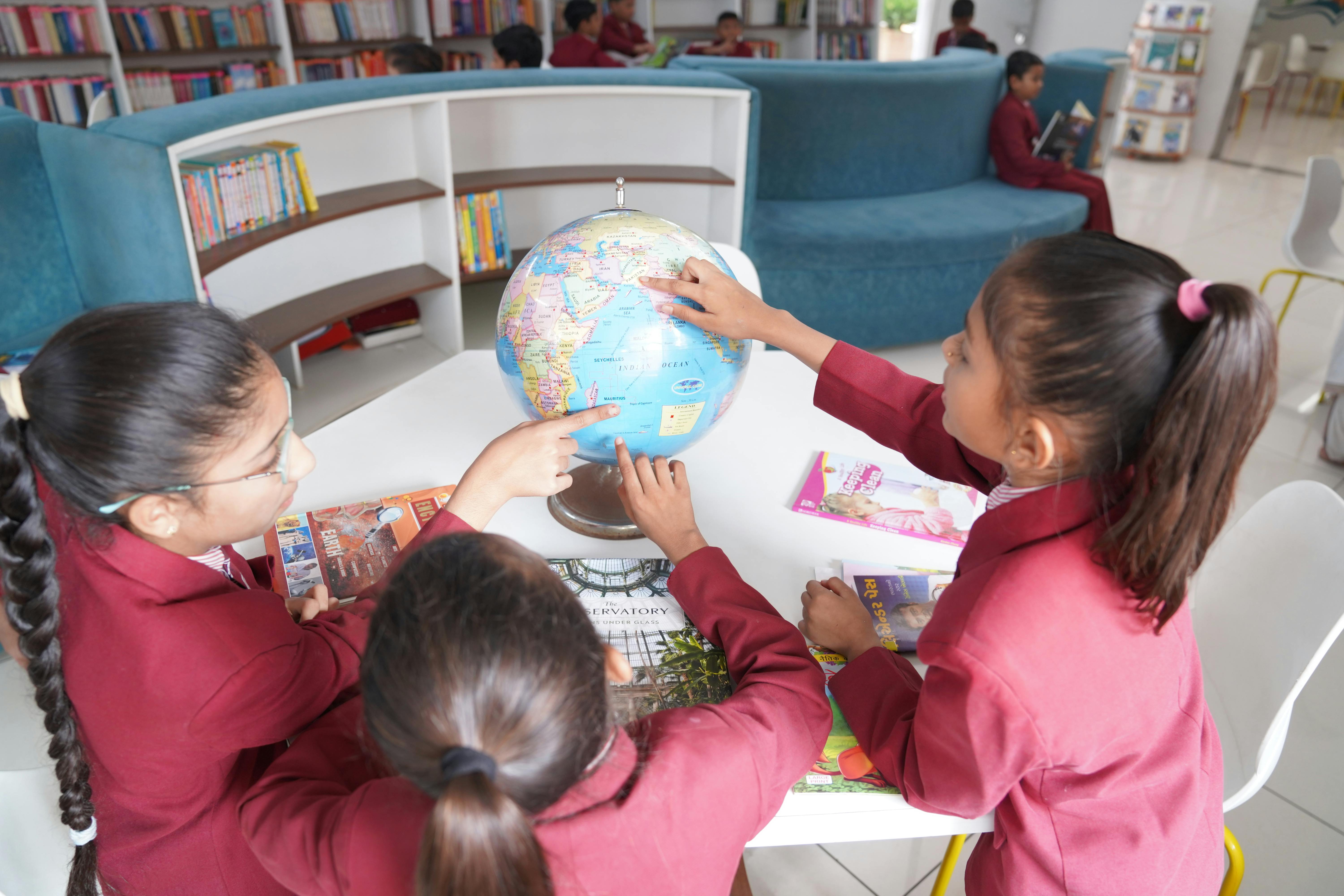 De franc Nens en uniforme aprenent geografia amb un globus terraqüi en una biblioteca contemporània. Foto d'estoc