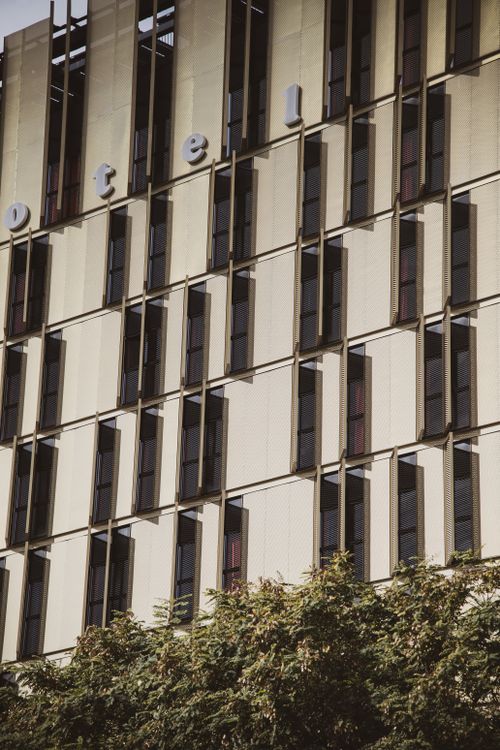 Free Modern hotel facade with geometric window design and greenery in foreground. Stock Photo