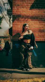 Confident woman in streetwear fashion posing against a brick wall in an urban setting.