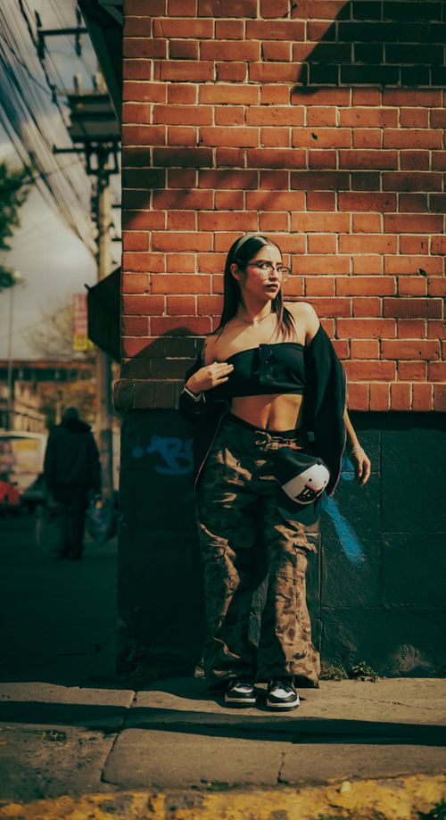 Free Confident woman in streetwear fashion posing against a brick wall in an urban setting. Stock Photo