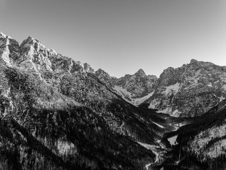 A stunning black and white landscape of the Julian Alps in winter, showcasing rugged peaks and snow-covered valleys.