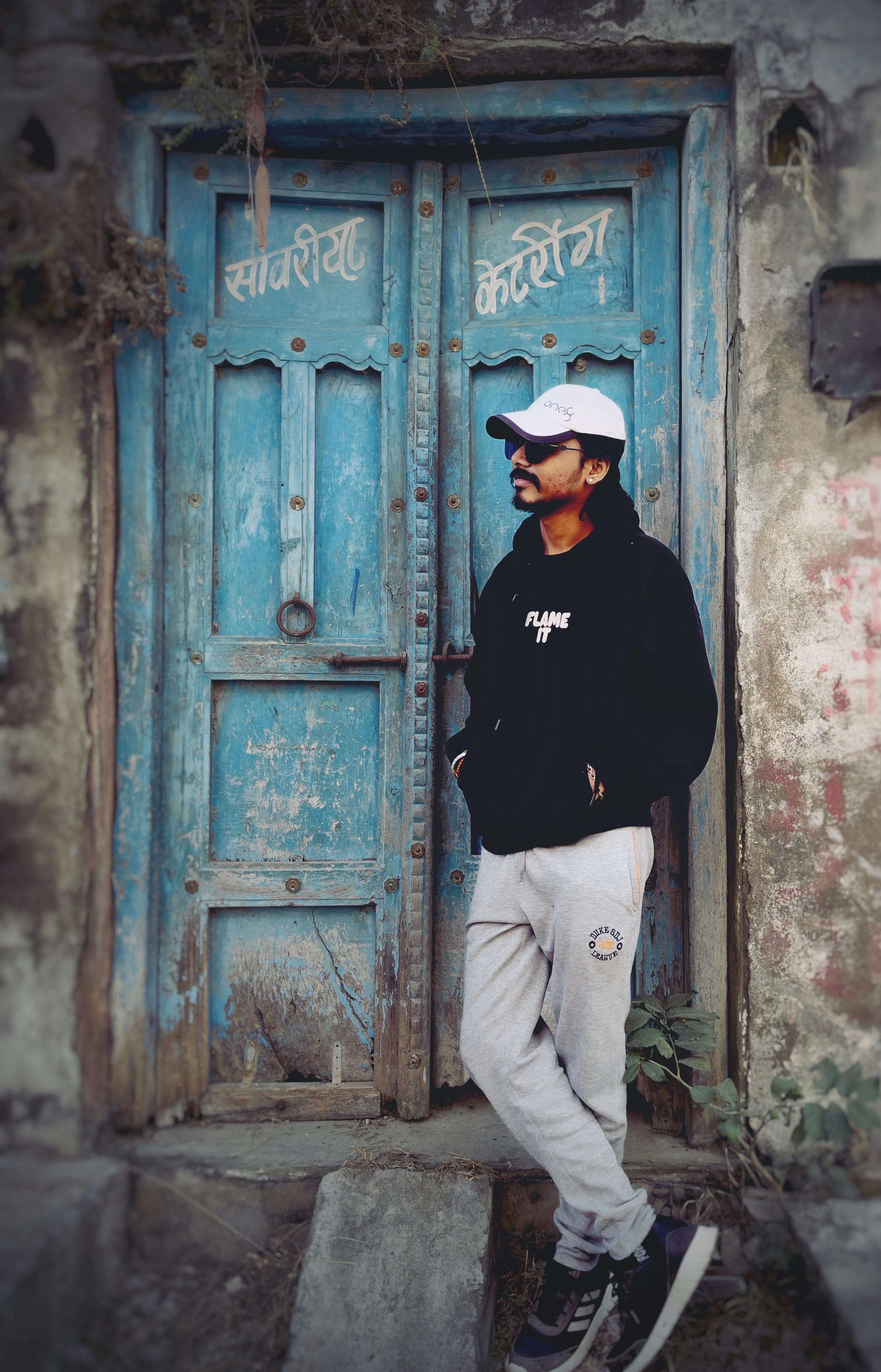 Free Man in casual streetwear leaning on a rustic door in Samriya, Rajasthan. Stock Photo