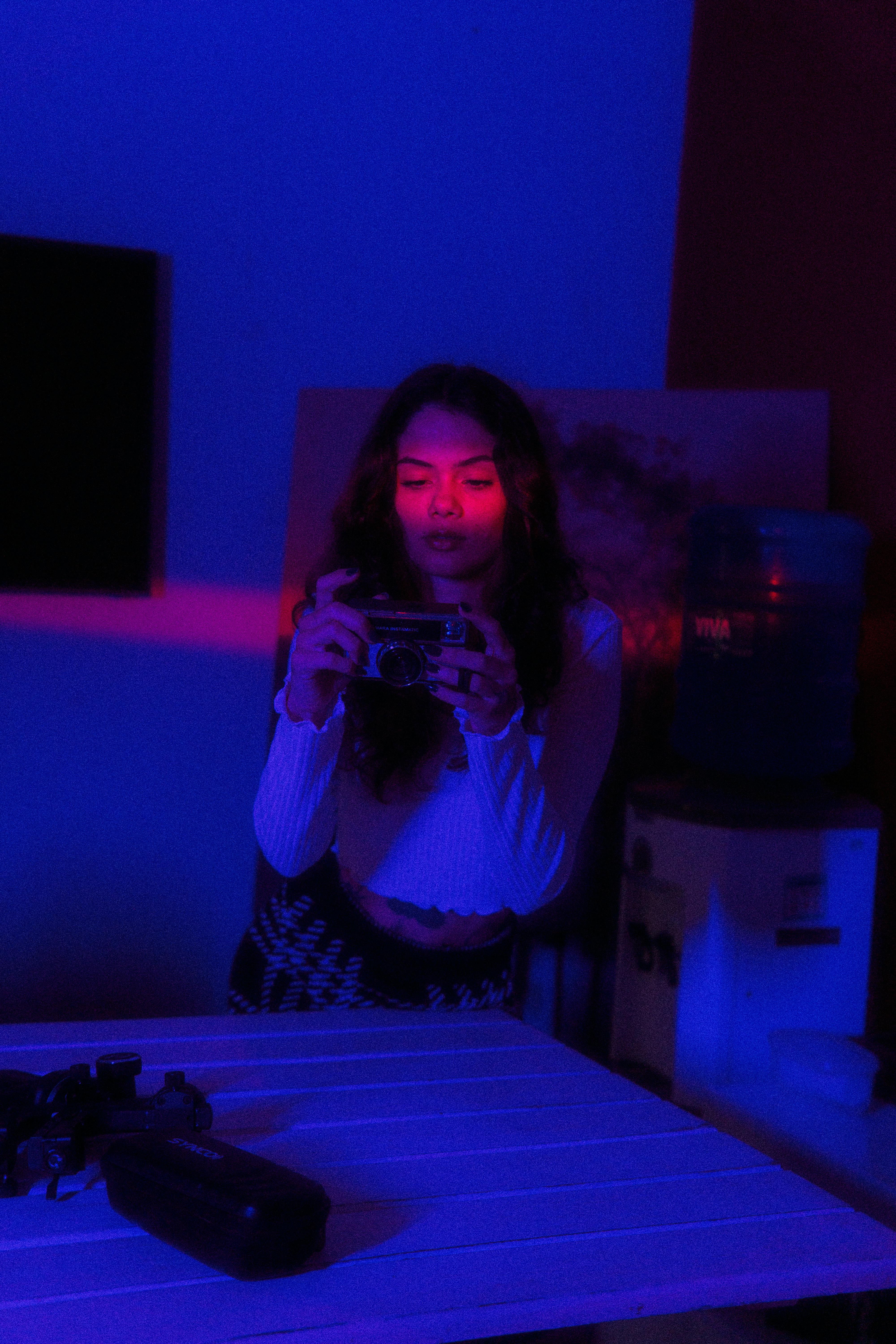 無料 ネオンパープルとピンクの照明の中でカメラを持った女性が、モダンで芸術的な雰囲気を醸し出しています。 写真素材