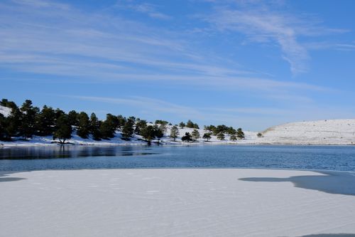 Free Serene winter vista of a snow-covered landscape and calm lake under a clear blue sky. Stock Photo